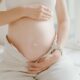 Primer plano de una mujer embarazada sosteniendo suavemente su vientre, simbolizando la maternidad y la maternidad.