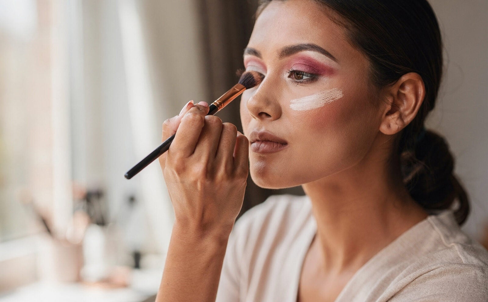 Persona genérica aplicándose maquillaje expresivo, gesto en curso, sin resultado final de look completo.
