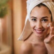 Mujer hermosa aplicando crema hidratante en su cara en el baño