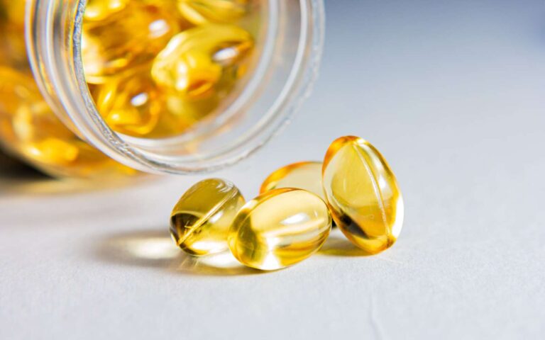 Primer plano de alta calidad de cápsulas de gelatina blanda transparentes derramadas de un frasco de vidrio, que muestran vitaminas o suplementos.