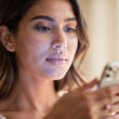 mujer con movil en la mano en primer plano con luz azul del movil reflejando sobre su cara, que el color genral de la imagen sea por el día y con luz natural