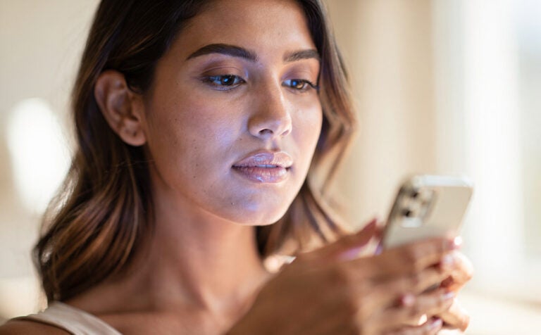 mujer con movil en la mano en primer plano con luz azul del movil reflejando sobre su cara, que el color genral de la imagen sea por el día y con luz natural