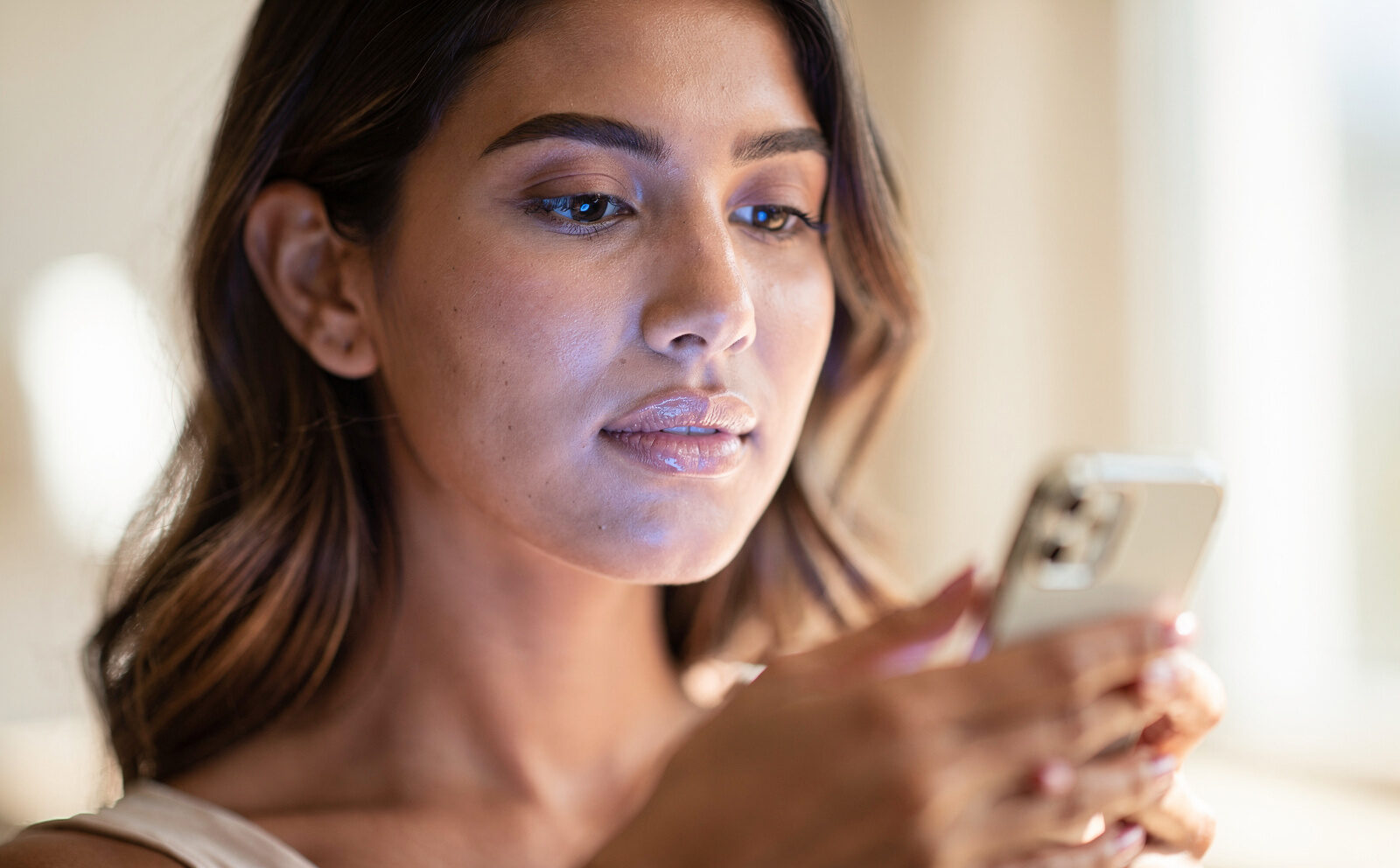 mujer con movil en la mano en primer plano con luz azul del movil reflejando sobre su cara, que el color genral de la imagen sea por el día y con luz natural