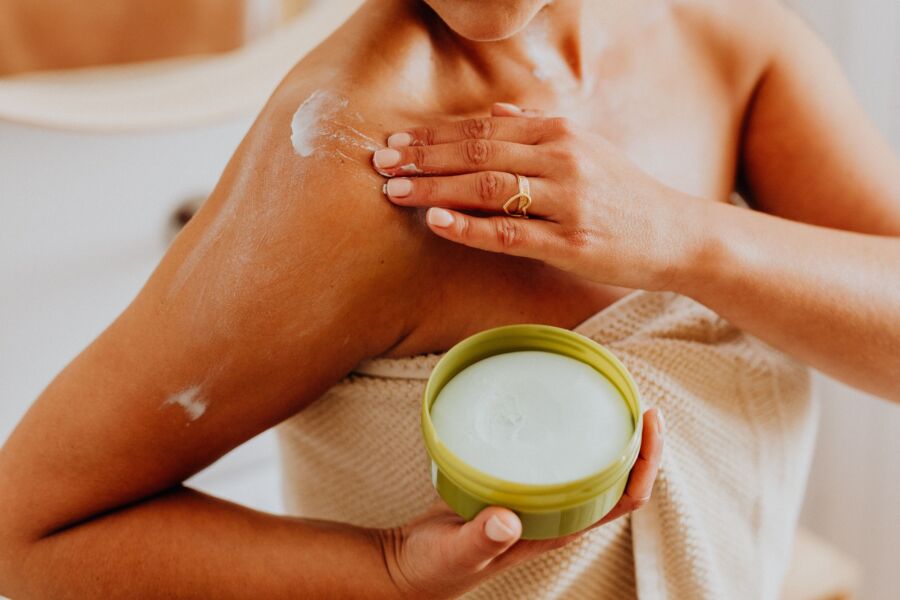 Primer plano de una mujer que se aplica crema en el hombro, centrándose en el cuidado de la piel y las rutinas de autocuidado.