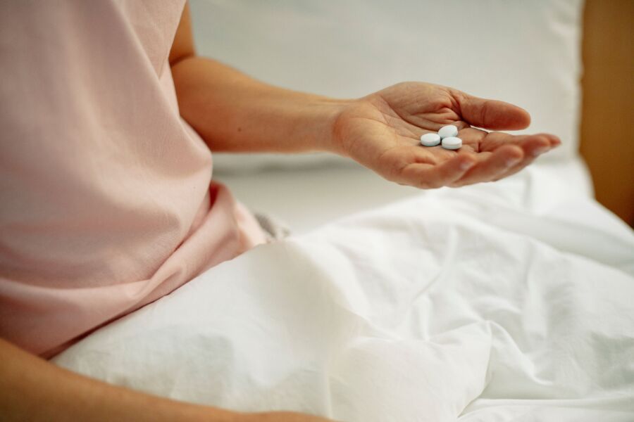 Recortar hembra anónima con pastillas en la mano en cama con sábanas blancas en hospital