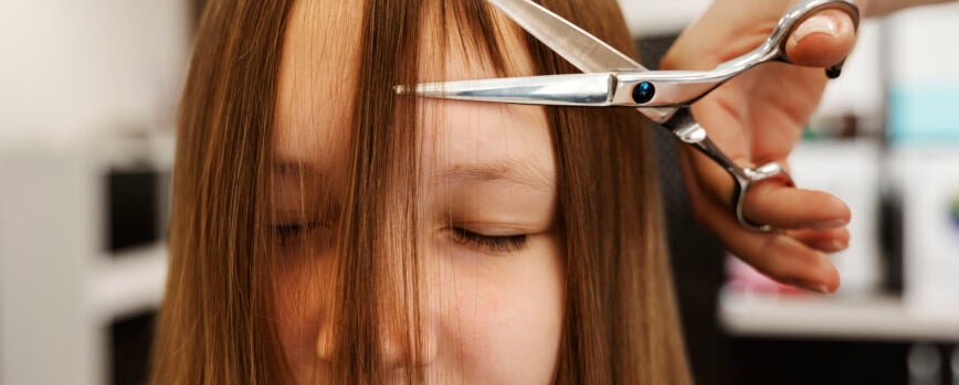 Chica de vista frontal cortándose el pelo en el salón