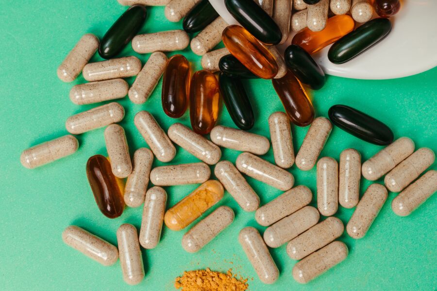 Varias píldoras y cápsulas esparcidas sobre una superficie verde, que simbolizan los suplementos para la salud.