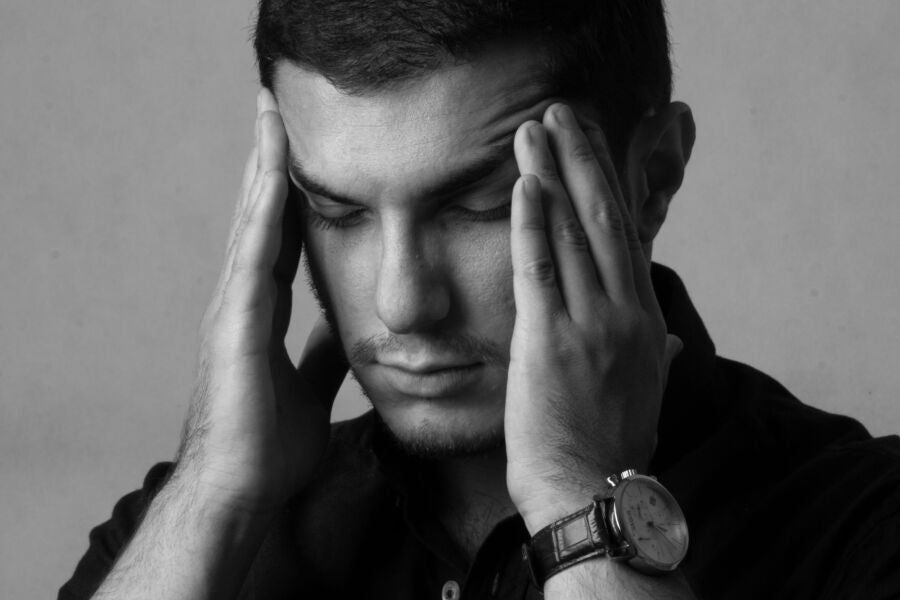 Retrato en primer plano en blanco y negro de un hombre sosteniendo la cabeza, lo que indica estrés o dolor de cabeza.