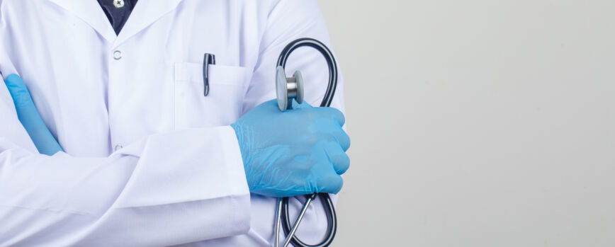 Médico cruzando los brazos mientras sostiene un estetoscopio en una bata blanca