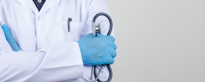 Médico cruzando los brazos mientras sostiene un estetoscopio en una bata blanca