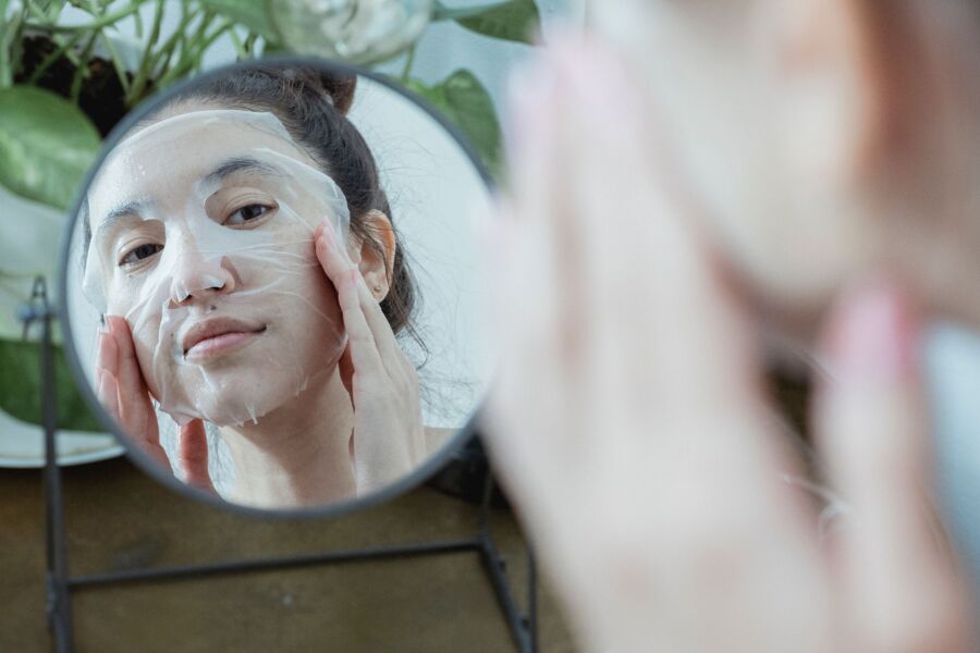 Una mujer frente a un espejo aplicando una mascarilla como parte de su rutina de cuidado de la piel.