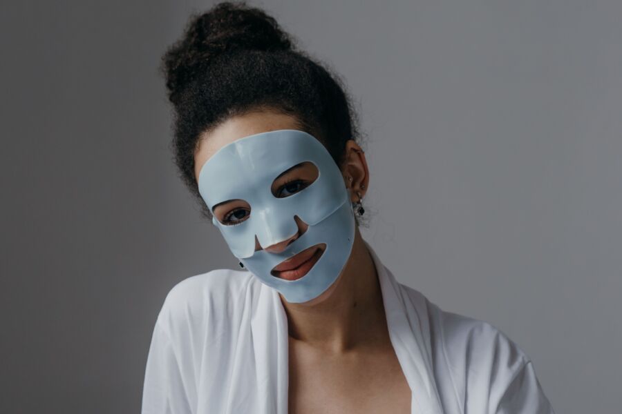 Mujer adulta disfrutando de una rutina de cuidado de la piel con una mascarilla de sábana azul en el interior.