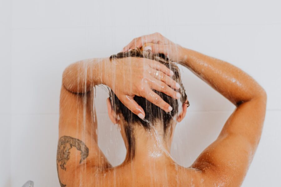 Persona duchándose, mostrando un tatuaje en el brazo y agua fluyendo hacia abajo.