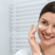Mujer sonriente en bata blanca con crema facial en el baño.