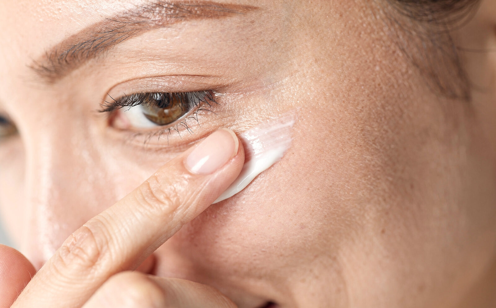 Gesto de aplicación del contorno de ojos con el dedo anular sobre la zona periocular, proceso en curso, nunca un resultado 'ojeras borradas' antes/después.