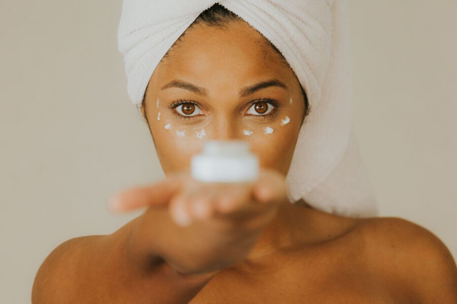 Primer plano de una mujer sosteniendo un frasco de crema facial centrándose en la práctica del cuidado de la piel.