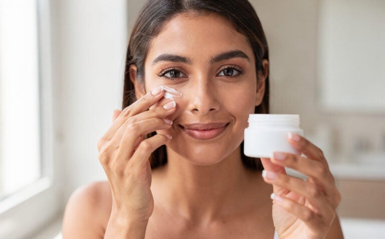 chica se pone crema en el contorno de los ojos y tiene en la mano el bote de crema