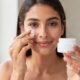 chica se pone crema en el contorno de los ojos y tiene en la mano el bote de crema