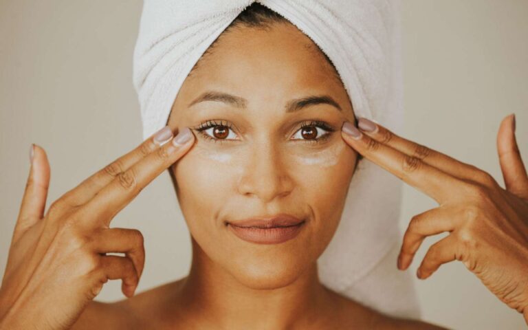 Mujer aplicando crema facial con una toalla envuelta en la cabeza, destacando rutina de cuidado de la piel.