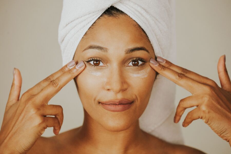 Mujer aplicando crema facial con una toalla envuelta en la cabeza, destacando rutina de cuidado de la piel.