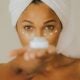 Primer plano de una mujer sosteniendo un frasco de crema facial centrándose en la práctica del cuidado de la piel.