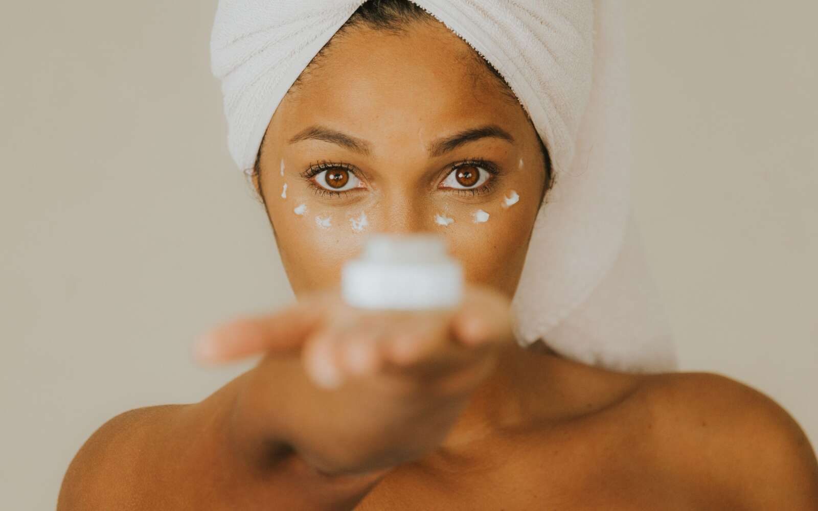 Primer plano de una mujer sosteniendo un frasco de crema facial centrándose en la práctica del cuidado de la piel.