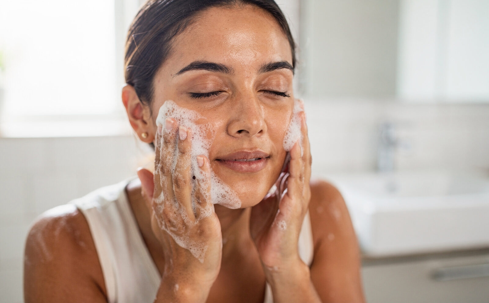 mujer se lava la cara con jabon facial