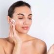 Retrato de belleza cercano de una mujer en topless con piel perfecta y maquillaje natural quitando almohadillas de algodón sobre un fondo blancox9