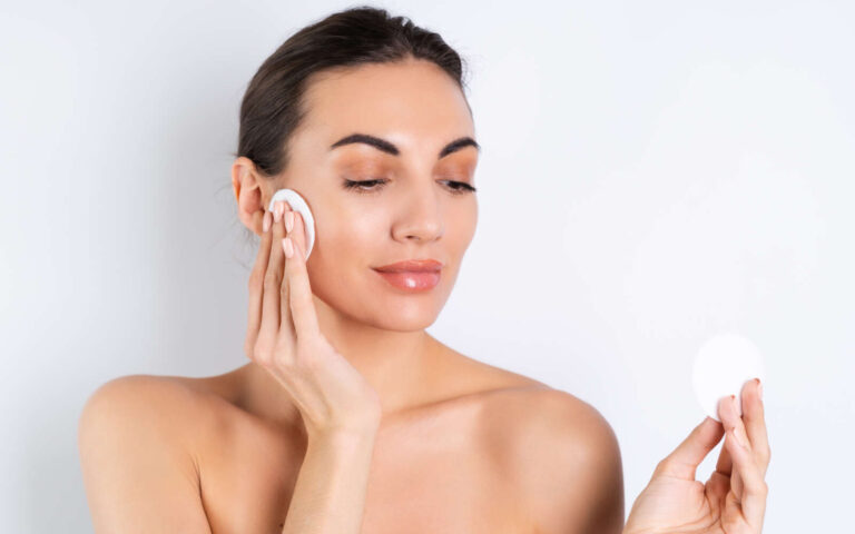 Retrato de belleza cercano de una mujer en topless con piel perfecta y maquillaje natural quitando almohadillas de algodón sobre un fondo blancox9