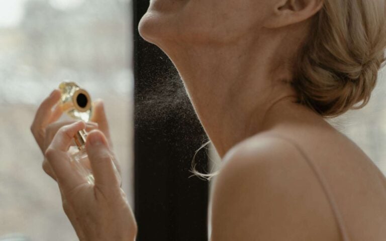 Primer plano de una mujer aplicando perfume con un frasco de vidrio con luz natural.