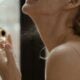 Primer plano de una mujer aplicando perfume con un frasco de vidrio con luz natural.