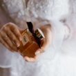 Una novia en vestido de encaje blanco con una botella de perfume Chloe de lujo, que simboliza la elegancia y el estilo.