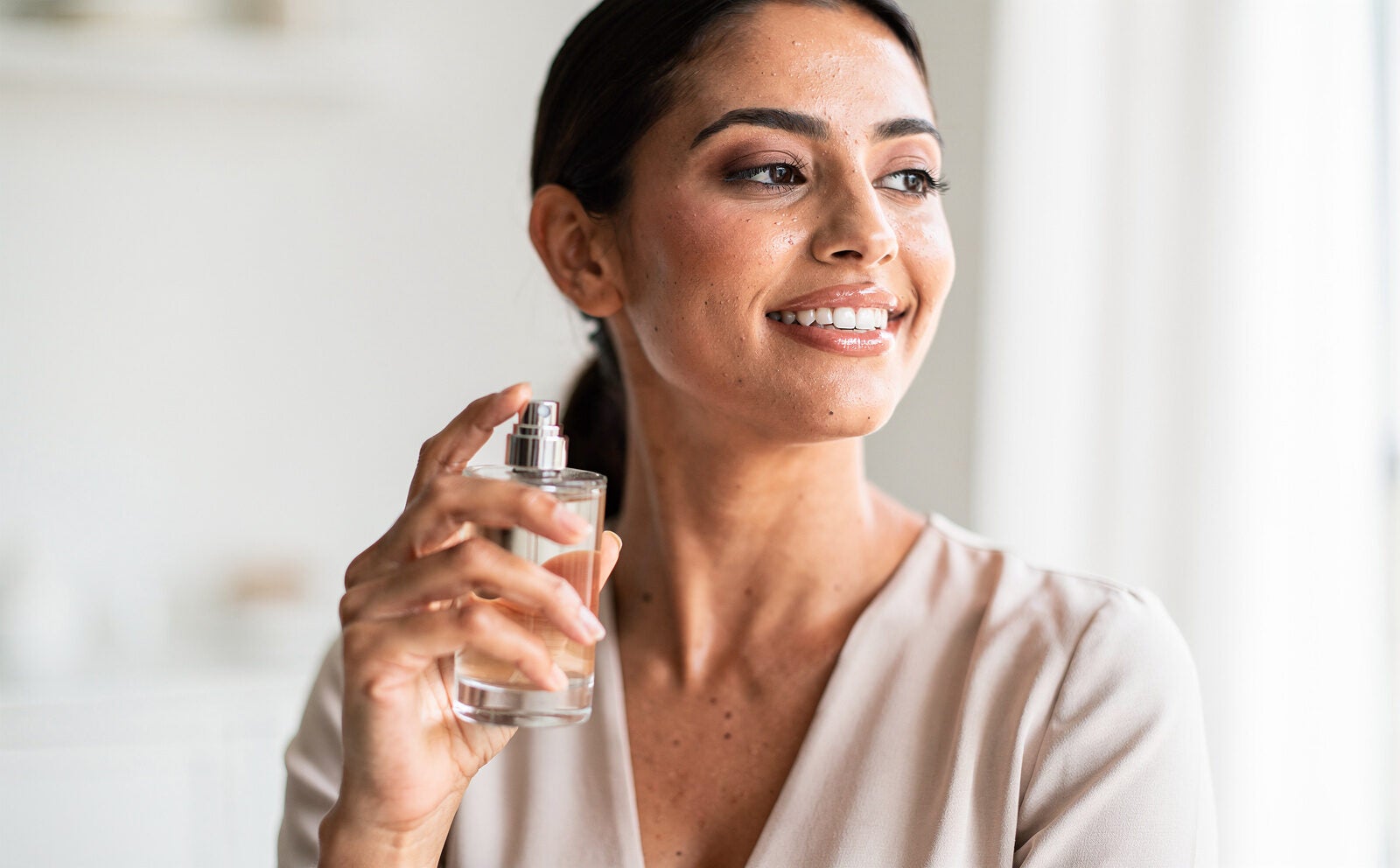 mujer estilosa y sofisticada se pone perfume, y sonrie