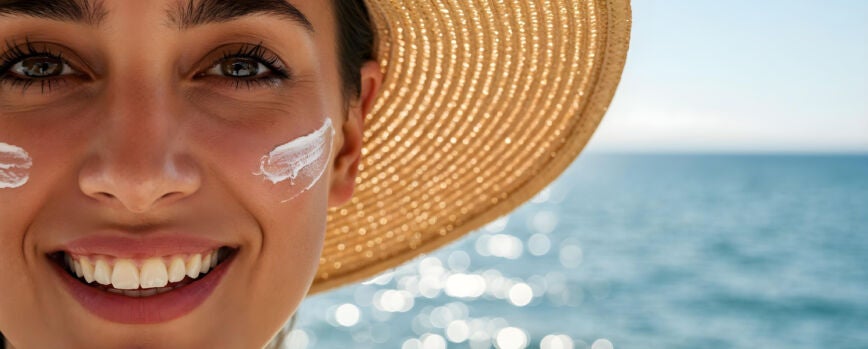 Mujer aplicando protector solar con una sonrisa en la playa