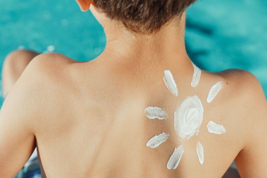Espalda del niño con protector solar en forma de sol, disfrutando de un día soleado junto a la piscina.