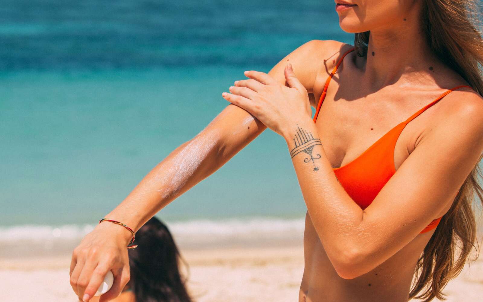 Una mujer en bikini aplica protector solar en una playa soleada, lo que garantiza la protección solar y el cuidado de la piel.