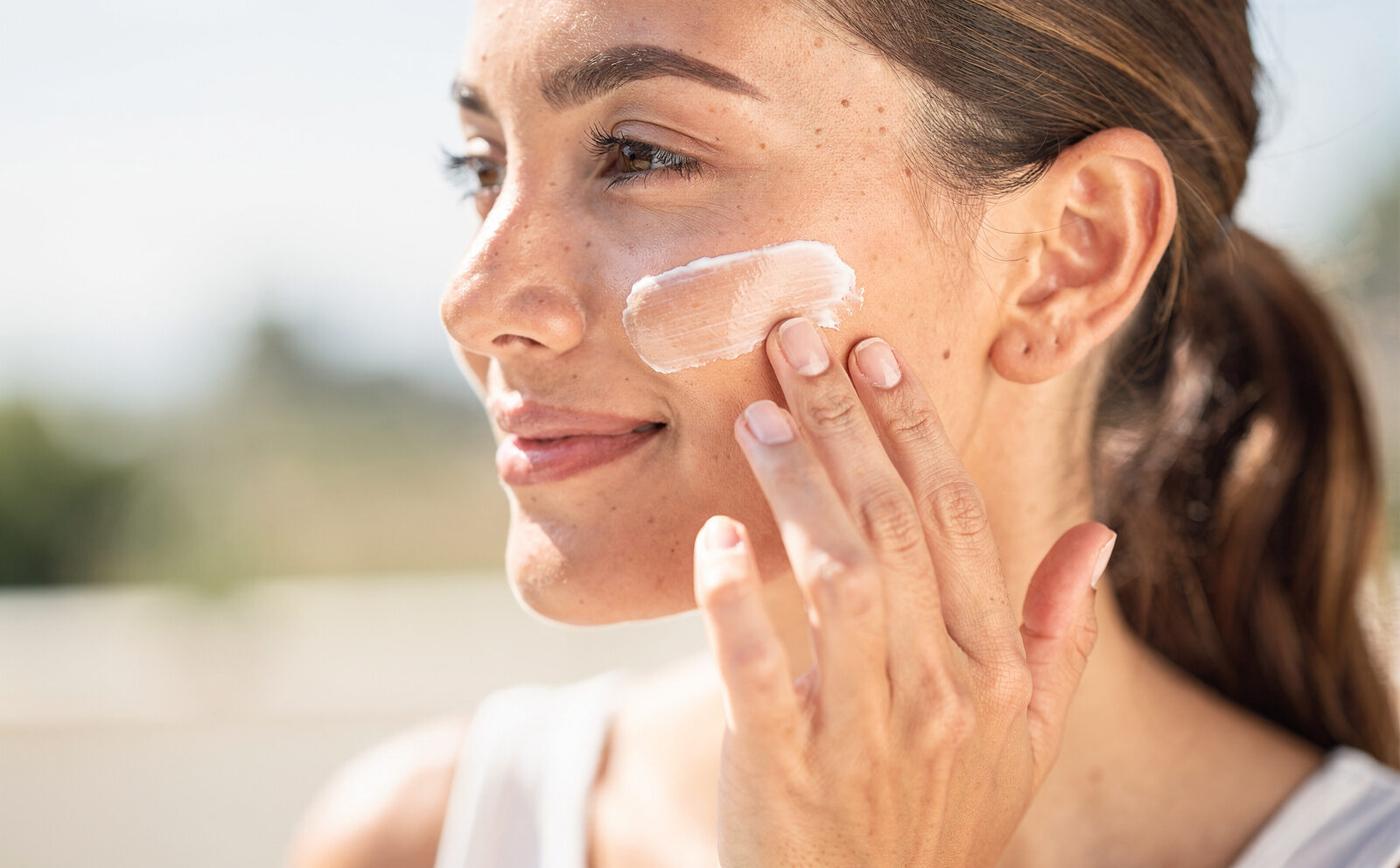 mujer poniendose protector solar en el exterior primer plano