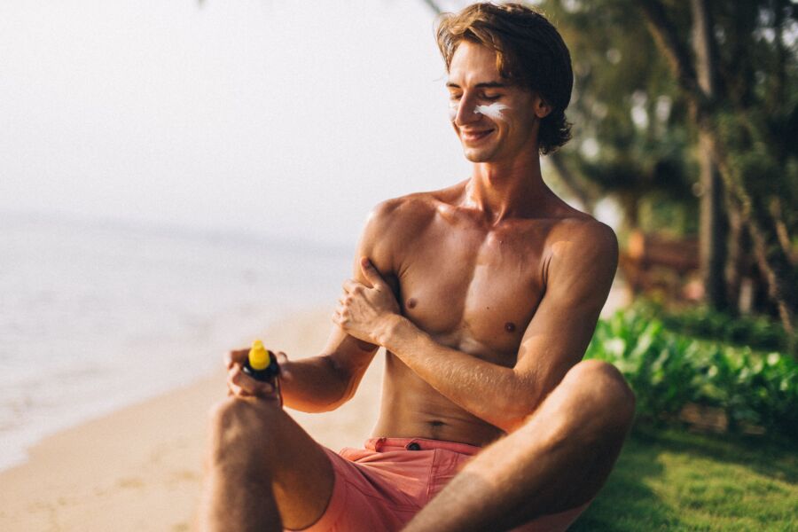 Hombre adulto aplica protector solar en una playa soleada, disfrutando de las vacaciones de verano.