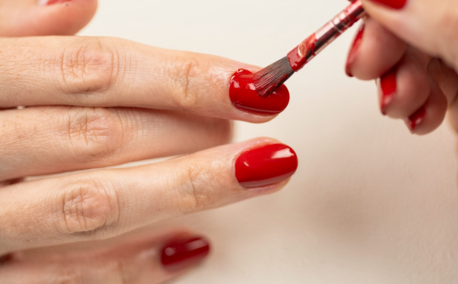 Aplicación de esmalte rojo sobre la uña, pincel en gesto; sin manicura terminada como foco ni celebridades.