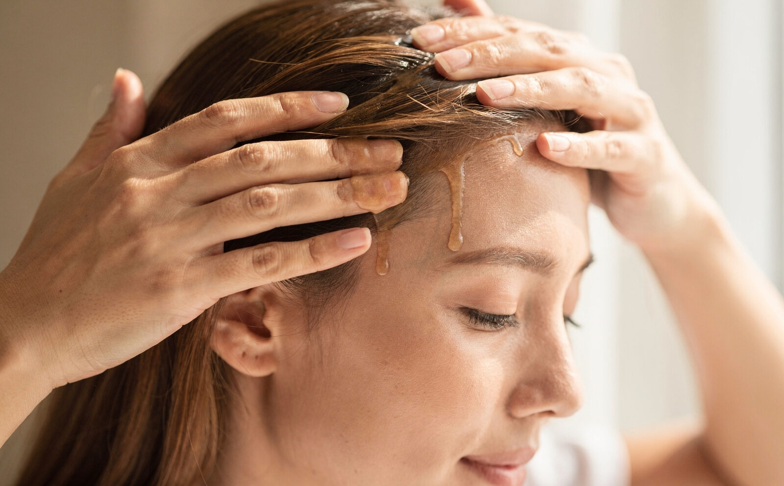 Persona aplicándose el sérum sobre el cuero cabelludo con gesto de masaje — proceso en curso, nunca comparación de cantidad de pelo antes/después.
