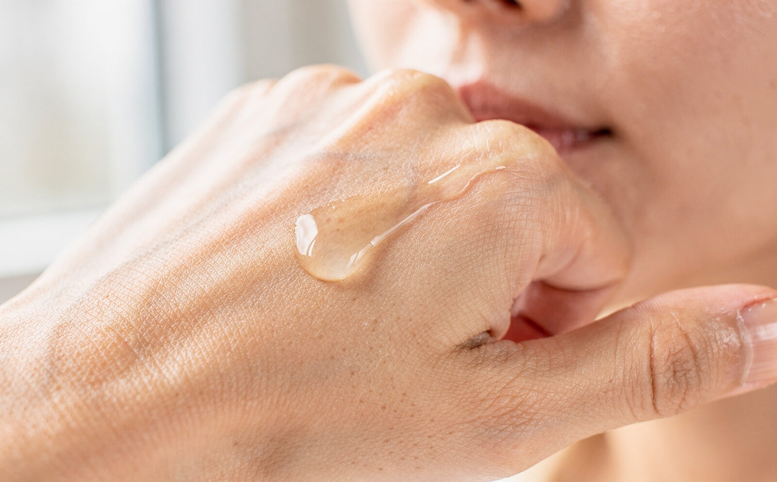 Gota de sérum sobre el dorso de la mano o aplicándose en el rostro, textura visible, sin resultado final ni celebridades.