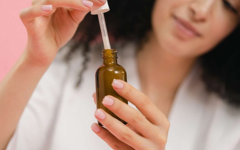 Primer plano de una mujer usando un biberón cuentagotas, centrándose en el cuidado de la piel y la rutina de belleza.