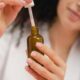 Primer plano de una mujer usando un biberón cuentagotas, centrándose en el cuidado de la piel y la rutina de belleza.