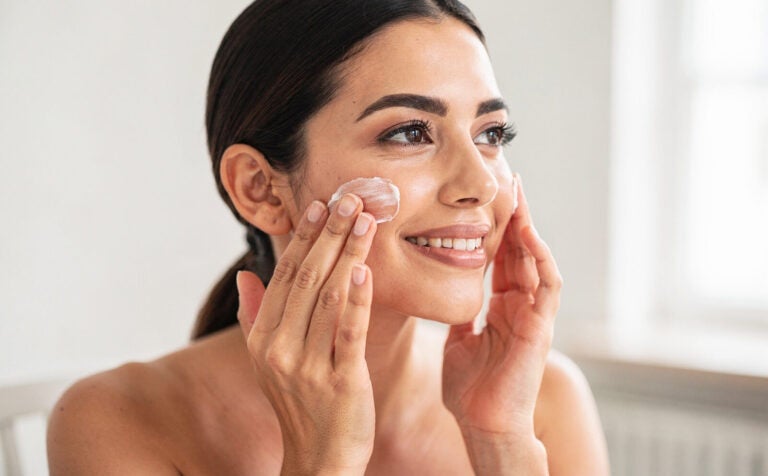 mujer se aplica crema facial en el rostro, sofisticada, sonriente
