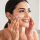mujer se aplica crema facial en el rostro, sofisticada, sonriente