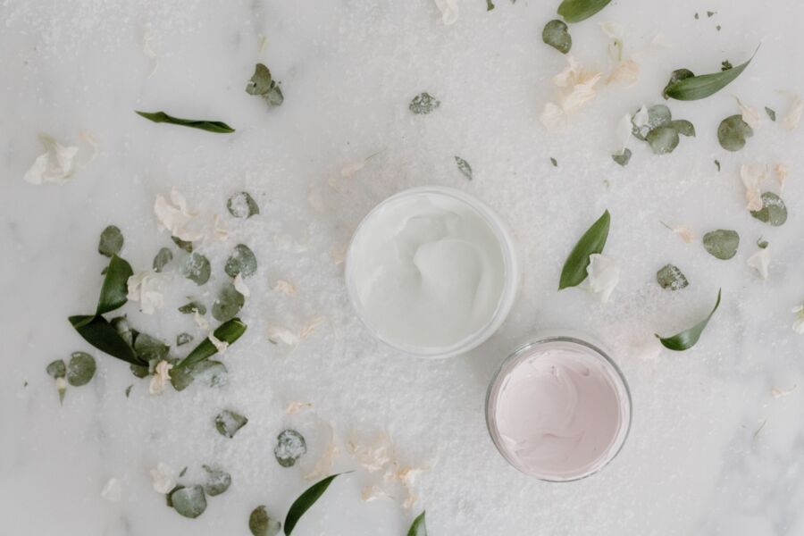 Colocación plana de tarros de crema cosmética rodeados de hojas y pétalos naturales, perfecta para promociones de productos de belleza.