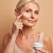 Hermosa mujer de mediana edad aplica crema antienvejecimiento en la cara se somete a tratamientos de belleza se preocupa por la piel