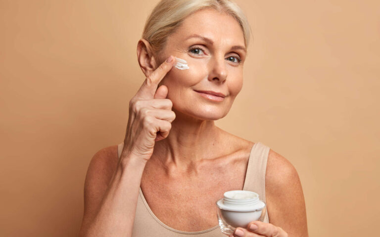 Hermosa mujer de mediana edad aplica crema antienvejecimiento en la cara se somete a tratamientos de belleza se preocupa por la piel