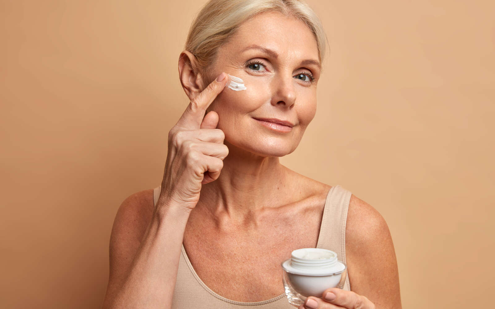 Hermosa mujer de mediana edad aplica crema antienvejecimiento en la cara se somete a tratamientos de belleza se preocupa por la piel