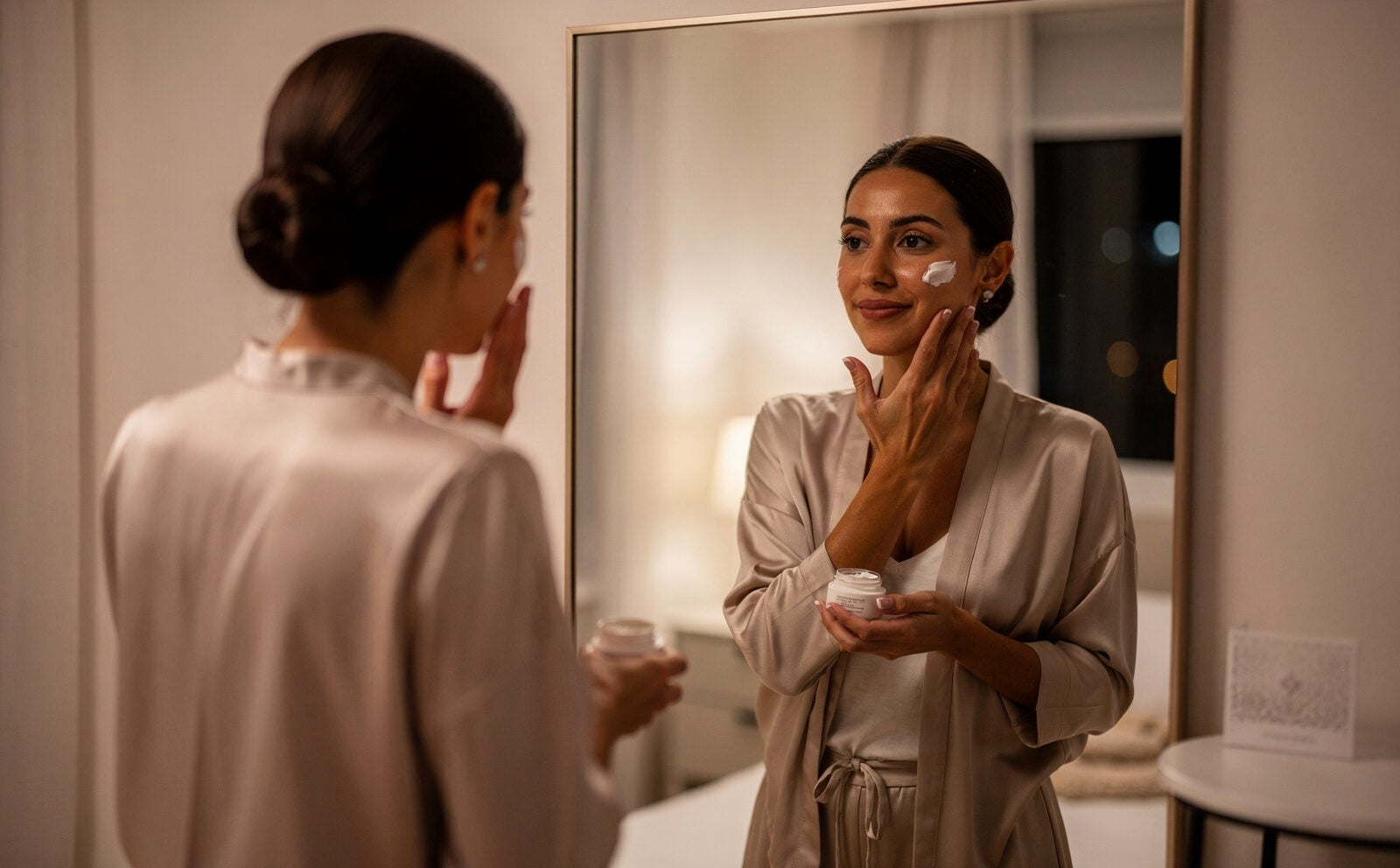 mujer sofisticada se pone crema facial en su habitacion de noche delante del espejo, plano medio, luz media de habiatacion